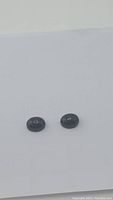 Two small natural jet black onyx oval cabochon stones shown side by side on plain white background.
