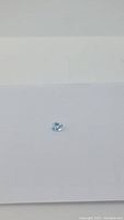 Photo of single oval cut light blue topaz gemstone on white background showing color and cut from above.