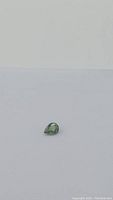 Loose pear-shaped green sapphire on white background, full view