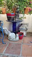 Blue glass-top bistro table with plant pots and garden statues placed around it.