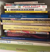Photo showing a stacked view of multiple art and graphic design books, mostly hardback and some softcover, titles visible include Keith Haring biography, pop art, and others.
