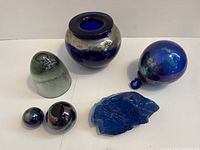 Full view of the six glass pieces showing the cobalt blue handblown vase, hanging ornament, large cobalt slab, and three smaller decorative glass pieces.