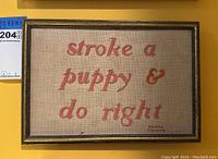 Frontal view of framed embroidered wall art showing stitched slogan and frame details.
