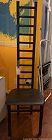 Front view of the black tall ladder back chair with leather seat showing the overall design and condition.
