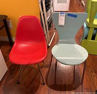Front view of two children's chairs side-by-side: red Eames-style and aqua/light blue Trento/Sienna-style chairs.