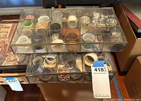Overhead view of two glass cases with multiple compartments containing assorted napkin rings of various materials and colors.