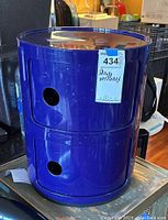 Front and angle views of the blue Kartell storage cabinet showing its cylindrical shape and the two cut-out circular handles on sliding compartments.