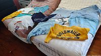 Overhead view of full assortment of 12 graphic t-shirts laid out on bed