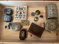 Overview of all assorted trinket and pill boxes in wooden crate showing varied materials including wood, marble, metal, and stone with detailed artworks and inlays