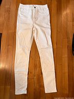 Front view of Cello white skinny jeans laid flat on wooden floor, showing button closure, pockets, and slim cut