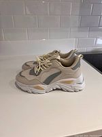 Side profile of the sneakers showing beige and gray color blocks and thick white sole.
