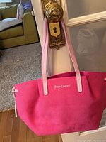 Front view of hot pink Juicy Couture tote bag with white logo and light pink handles hanging on door handle.