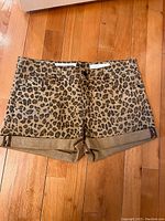 Leopard print jean shorts laid flat on wooden floor showing front view with rolled cuffs.