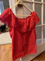 Red blouse hanging on a wooden hanger showing the off-shoulder wide eyelet lace neckline