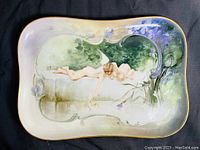 Front view of the Limoges porcelain tray showing the hand-painted cherub waterside scene with floral edge decorations and gold trim.