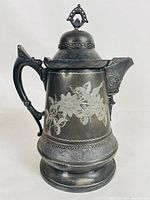 Side view of antique silverplate ice pitcher showing floral engravings and ornate handle