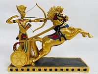 Side view of golden cast resin figurine showing pharaoh drawing a bow on a chariot pulled by a rearing horse.
