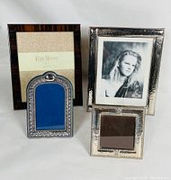 Four picture frames displayed, three EPNS silver plated frames with detailed etched patterns and one wood frame with polished dark grain finish, all shown from front with easel backs visible