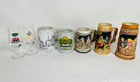 Full view of the six beer glasses and steins lined up, showing logos, colors, and details.
