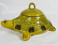 Front-side view of yellow ceramic turtle soup tureen with lid showing detailed patterns and handle.