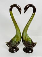 Front view of pair of matching vintage ceramic heron figurines, showing long curved necks and green to brown glaze.
