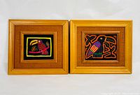 Pair of framed Cuna Mola textile art pieces, each with a colorful bird design on fabric with woven backing and wooden frame, displayed side by side.