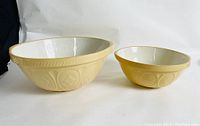 Two yellowware nesting mixing bowls shown from front, highlighting embossed patterns and white glazed interior.
