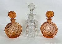 Front view of three vintage glass stopper bottles: two amber swirl pattern bottles and one clear cut glass bottle with faceted stopper.