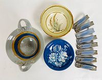 Front view of pottery pieces including handled pot, two bowls, and 10 napkin rings arranged on white surface.