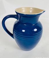 Front and side views of the cobalt blue Le Creuset pitcher with beige interior, showing its shape, handle, and spout.