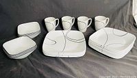 Photo showing the full set of stacked bowls, plates, mugs, and rectangular serving dishes all featuring black curved line patterns on white Mid-Century Modern Corelle dinnerware.