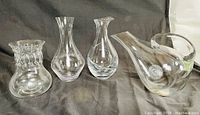 Five Mid-Century Modern clear glass vases and pitchers, arranged on black fabric, showing overall lot contents and condition.