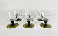 Six vintage stem glasses with clear tops and dark green bases arranged in rows on a white surface, shown from a top-front angle.