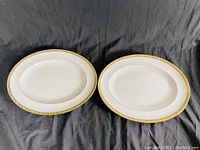 Two Wedgwood Marina bone china platters side by side on a dark cloth background showing size and detailing of decorative gold and green trim.