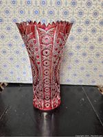 Front view of deep red crystal vase with intricate etching and scalloped rim.