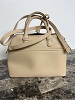 Front and side view of the light brown handbag showing shape, handles, and shoulder strap.