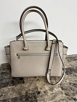 Front view of light beige lady's tote bag with handles and shoulder strap, placed on a stone surface