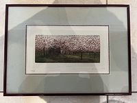 Framed lithograph with mat showing a stone cottage and flowering trees in muted colors.