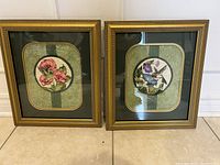Front view of the pair of vintage embroidery framed art pieces showing floral and bird designs with gold-tone frames and green mats.