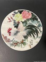 Top-down view of a round marble plate showing two painted chickens surrounded by flowers and Asian script.