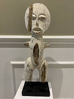 Front view of the man-shaped wooden sculpture showing white textured surface with exposed wood and facial features.