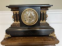 Full view of the antique mantel clock showing its black case, gold decorative details, and faux marble columns.