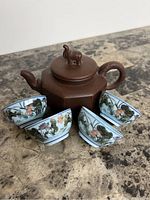 The full set including the brown hexagonal teapot with elephant knob lid and four floral porcelain tea cups arranged around it on a marble surface.