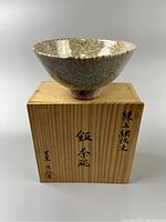 Antique Japanese bowl displayed on wooden box with Japanese kanji inscriptions, showing overall item and storage box.