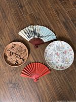 Overview of all four items together on floor: carved wood plate, two folding fans, porcelain plate