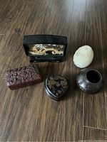 Overview of five assorted antique items placed on wooden floor: carved lacquer boxes, carved stone egg, small dark vase, and framed carved Asian scene.