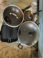 Overhead photo showing two cooking pots with glass lids and a ribbed grill pan with metal handle.