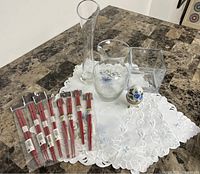 Photo of three clear glass vases, porcelain egg decoration with butterfly motif, and red chopsticks on white embroidered cloth.