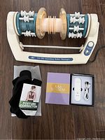 Photo showing foot massager with white plastic frame, blue-green rollers, power cord, black posture corrector strap and packaging for UV sterilizer device with USB cable