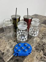 Overview of the two stainless steel Starbucks cups with straws, three clear glass lidded bottles with white triangle patterns, and blue handheld massage pad.